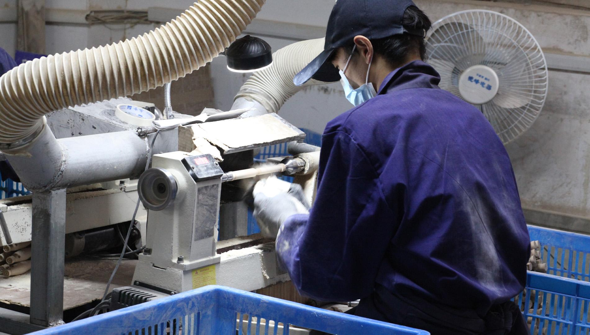 A factory worker polishing a wooden brush component at a machine