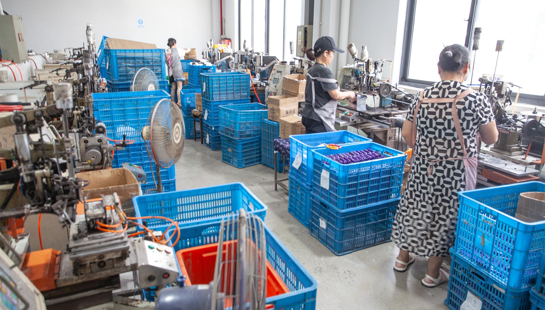 Workers operating brush tufting machines beside blue production baskets